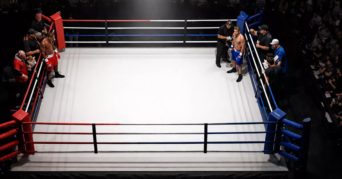 Vista cenital de un ring de boxeo iluminado con dos púgiles preparados para el combate